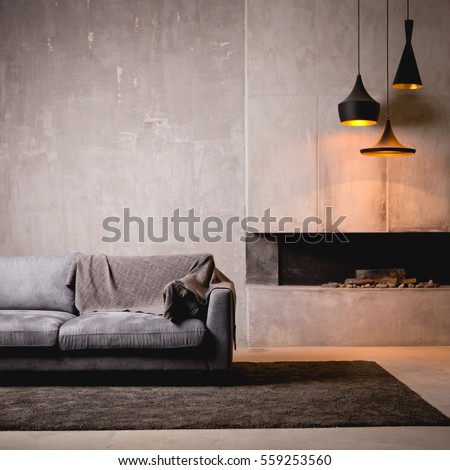 Gray velour sofa in a dark room the bright light from eternal light, and artificial fireplace. Interior loft with concrete walls