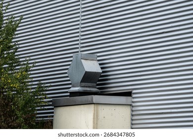 A gray ventilation unit is mounted on top of a white container beside a corrugated metal wall. Surrounding vegetation adds a touch of greenery to the industrial setting.