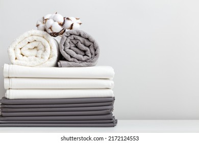Gray white bed linen, a sheet and two rolled up towels on the table.