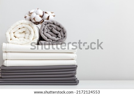 Gray white bed linen, a sheet and two rolled up towels on the table.