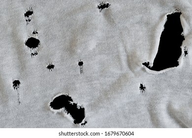 Gray white fabric with many holes. Texture of an old dirty ragged t shirt. Grunge damaged cloth on black background. Crumpled torn rag. Copy space