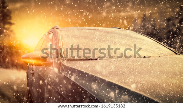 Gray winter car cover of frost and\
snow flakes.Winter landscape of forest and sunset time.Free space\
for your decoration. Cold december car trip\
