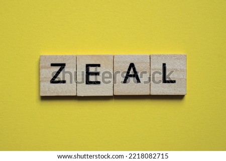 the gray word zeal of gray small wooden letters lies on a yellow table
