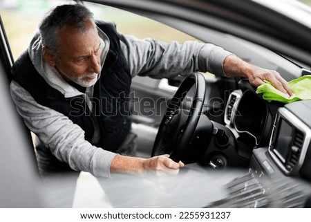 Gray-haired bearded Caucasian 60-70 years old elderly man, washing his car at a self service car wash station. He's using the microfiber towel, polishing and waxing the car dashboard and interior. Foto stock © 