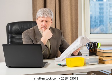 Gray-haired Businessman Is Working In Office. Man Lawyer At Workplace. Concept - Employee Of A Legal Bureau. Employee Of A Law Firm. Lawyer Looks At Laptop. Legal Business. Legal Career.