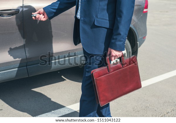 Gray-haired middle aged\
businessman in a blue suit and briefcase pushing button on remote\
control car key