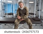 Gray-haired military man sits in the gym of rehabilitation center