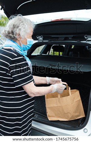 gray-haired old woman +80, in a medical mask puts goods into the trunk floor

Lady in medical mask, hands in latex gloves,
Concept: Purchase of products, goods, protection against coronavirus