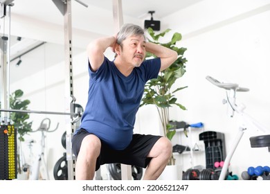 Gray-haired senior man doing squats at the gym
				