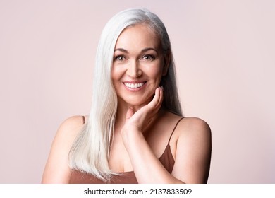 Gray-haired woman looking at camera. Positive single mature senior retired woman touching healthy groomed perfect face skin. Natural old beauty and aging concept.