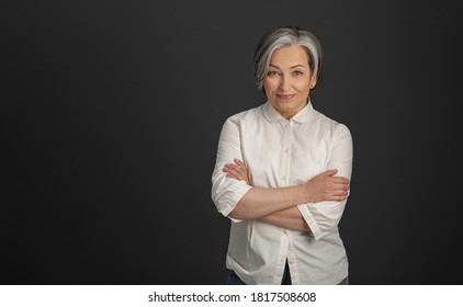 Graying Pretty Woman In White Shirt Stands Arms-crossed Isolated On Dark Gray Background. High Quality Photo.