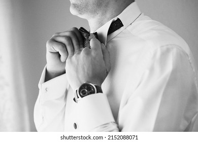 A Grayscale Closeup Of A Faceless Groom Fixing His Bowtie On The Wedding Day