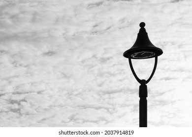 A Grayscale Closeup Shot Of A Forged Streetlight With Cloudy Sky In The Background