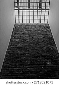 Grayscale interior of a tall rustic brick wall with a geometric glass skylight. Industrial loft architecture style with dramatic contrast and natural overhead lighting background.