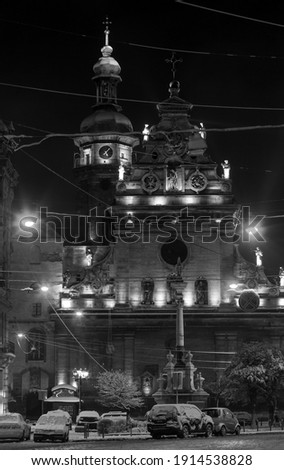 Grayscale. Night winter Lviv city (Ukraine) cityscape. Bernardine Church and monastery (church of St. Andrew) top, built in17th century. And Monument to Saint John of Dukla ahead, built in 1736.