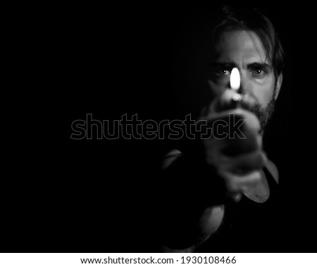 A grayscale portrait of an adult male holding a lighter in front of his face against a dark background
