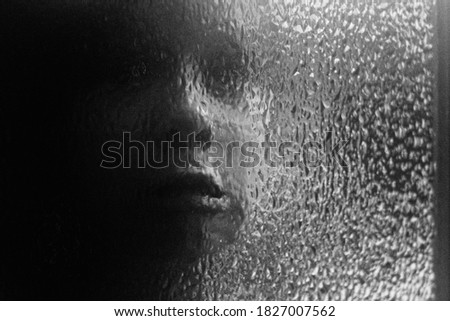 Grayscale portrait of ghost in wall close-up. Horror background with scared face behind glass. Silhouette of screaming ghost in window in darkness. Scary ghost in monochrome film style with grain.