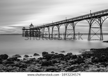 A grayscale shot of a bridge over a lake and stones on the bay on a cloudy da
