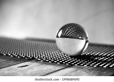 A grayscale shot of a glass lens ball on a black metal grid