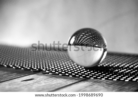A grayscale shot of a glass lens ball on a black metal grid