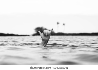 A grayscale shot of a hand on the surface of a lake showing a Decompression sign for divers