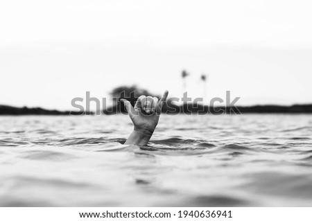 A grayscale shot of a hand on the surface of a lake showing a Decompression sign for divers