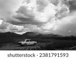 A grayscale shot of an old abanoned car parked in a vast desert landscape