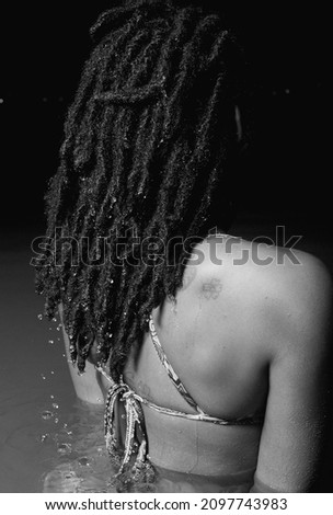 A grayscale shot of a Rasta woman with curly hair in a swimsuit in the water