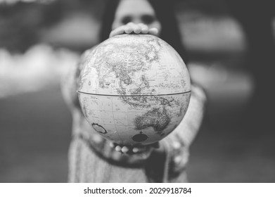A grayscale shot of a young Caucasian female holding a globe figure