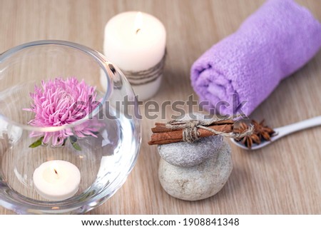 Graystones on top of each other, a candle, a lilac rolled towel, a vase of water with a lilac flower and candles floating in the water, cinnamon and star anise. Spa setting concept. Soft focus