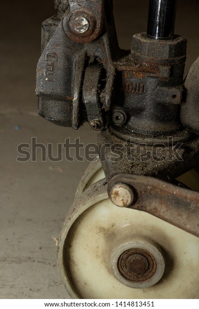 Grease\
covered hydraulic trolley in an industrial factory environment with\
yellow painted metal on dirty grimy wheels bearings rusted handle\
trolley machine operated by workers close\
up
