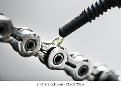 Greasing a bicycle chain with a drop of golden oil close-up on a gray background. Taking care of the bike drive system.