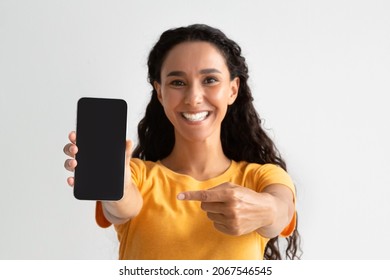 Great App. Cheerful Millennial Woman Pointing At Smartphone With Black Screen In her Hand, Smiling Young Lady Recommending New Mobile Application Or Website, Mockup Image With Copy Space