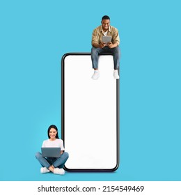 Great App. Excited Black Guy And Lady Sitting On Big Giant Smartphone With Blank White Screen Using Gadgets, Cheerful Couple Chatting On Social Media, Blue Wall, Mock Up. Modern Communication Concept - Powered by Shutterstock