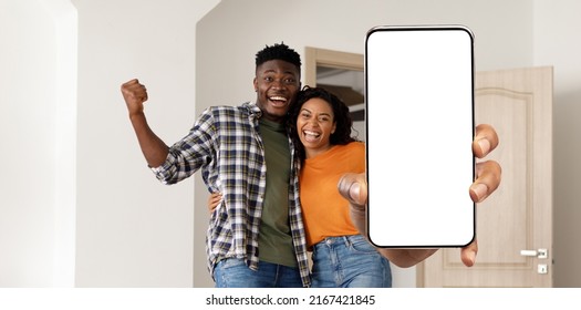 Great App. Portrait Of Cheerful Young Black Couple Holding Smartphone With Blank Screen While Standing In Room At Home, African American Spouses Showing Device With Copy Space For Mobile Mockup