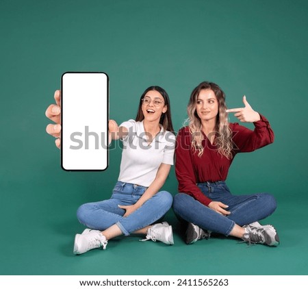Great application advice. Full length body view sitting cheerful caucasian woman friends recommending mobile app. Show empty screen mobile phone mock up. Pointing finger. Advertising website concept.