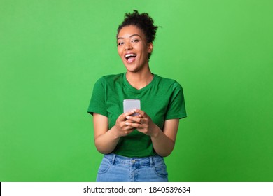 Great Application Or Website. Portrait Of Excited African American Woman Using Her Mobile Phone, Isolated On Green Studio Background, Copy Space. Positive Black Lady Holding Gadget, Looking At Camera