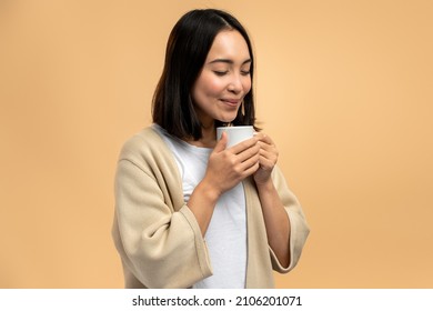 Great aroma. Waist up portrait view of the asian woman enjoying hot steaming beverage and inhaling coffee while posing over beige background  - Powered by Shutterstock