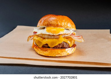 Great Beef Burger on Shiny Bun with Fried Egg, Sliced Bacon, Melted Dripping Cheddar Cheese, Sliced Cooked White Onion on Brown Greaseproof Paper - Powered by Shutterstock