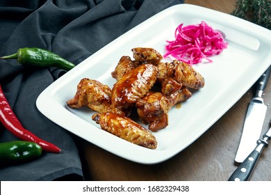 Great beer snack - spicy baked buffalo wings. BBQ wings with garnish of salad on white plate. Close up. Pub food