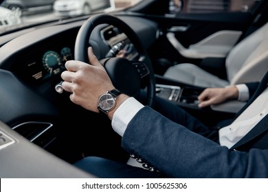 Great car. Close up top view of young man in formalwear keeping hand on the steering wheel while driving a luxury car