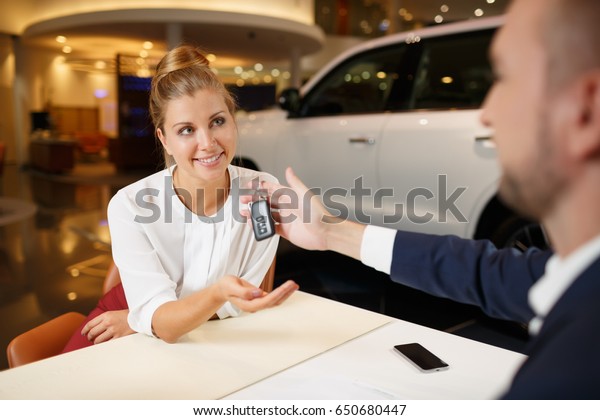 Great choice.\
Car salesman giving the key of  new car to the young attractive\
female customer at\
dealership