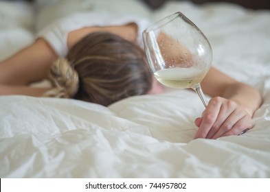 Great Concept Of Alcohol Abuse. Young Woman, Blond Hair, Fainted In Bed After Drinking Too Much Alcohol. Glass Of Wine In Hand, Bottle Of Wine.