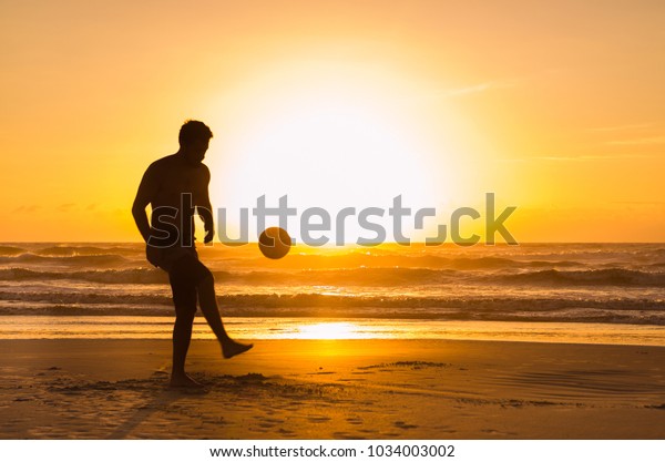 Great concept of soccer, man\
playing soccer on the beach in golden hour, sunset. Making keepie\
uppie.