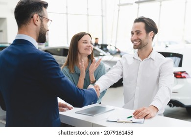 Great deal! Profitable deal handshake after buying purchasing new car. Male shop assistant congratulating young family couple with buying auto at dealer shop.