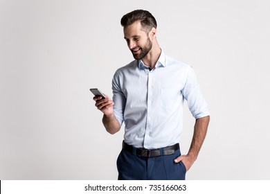 Great Email! Handsome Young Man Using His Phone With Smile While Standing Against White Background.