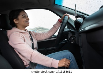 Great Friendly Taxi Driver, Auto Blogger And Car Traveler. Smiling Millennial African American Woman Holding Steering Wheel, Changing Speed, Looking At Road, Driving Car In Rain, Profile, Empty Space