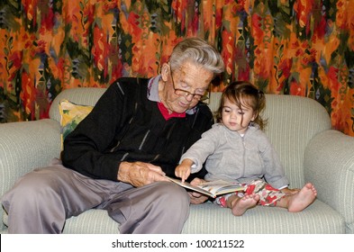 Great Grandad Reads A Book To His Great Grandchild On A Coach. Concept Photo Of Grandparents, Grandchild, Childhood, Relationship, Lifestyle,family, Education,active Seniors. Real People. Copy Space