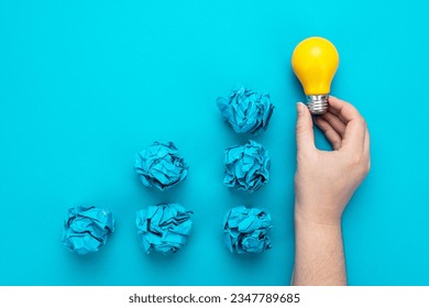 Great idea concept with bulb in hand and crumpled office paper. Conceptual photo of light bulb in human hand over turquoise background. One person have great idea during brainstorming session concept. - Shutterstock ID 2347789685