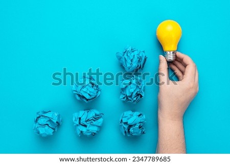 Great idea concept with bulb in hand and crumpled office paper. Conceptual photo of light bulb in human hand over turquoise background. One person have great idea during brainstorming session concept.